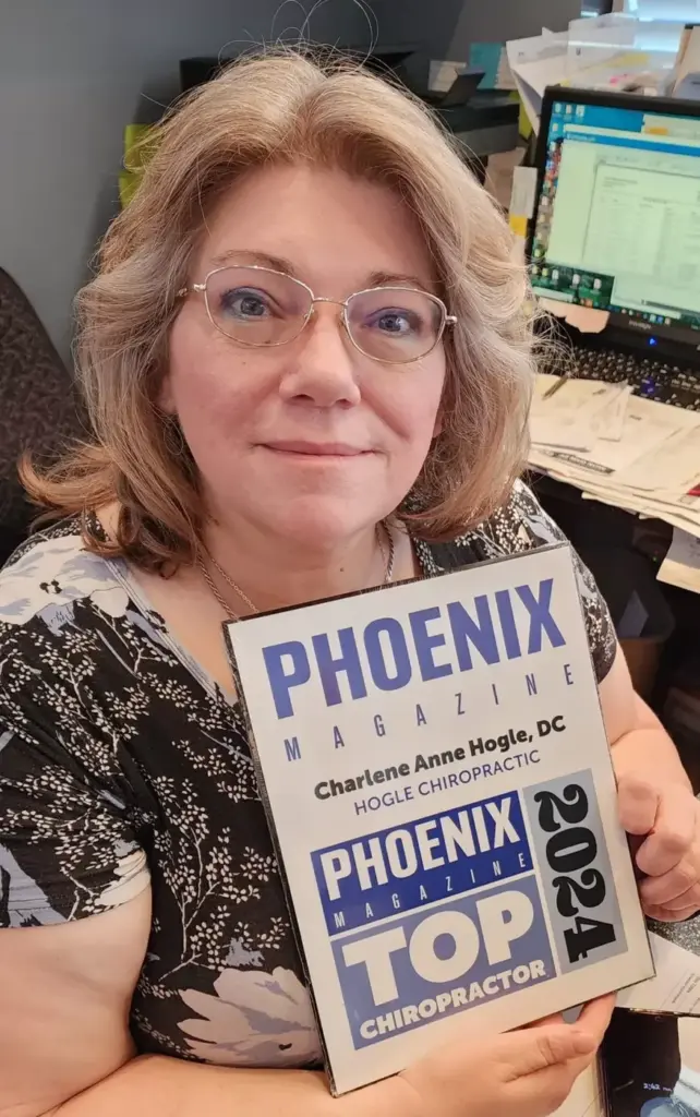 Dr. Charlene Hogle smiling at her desk, holding her Phoenix Magazine Top Chiropractor 2024 plaque