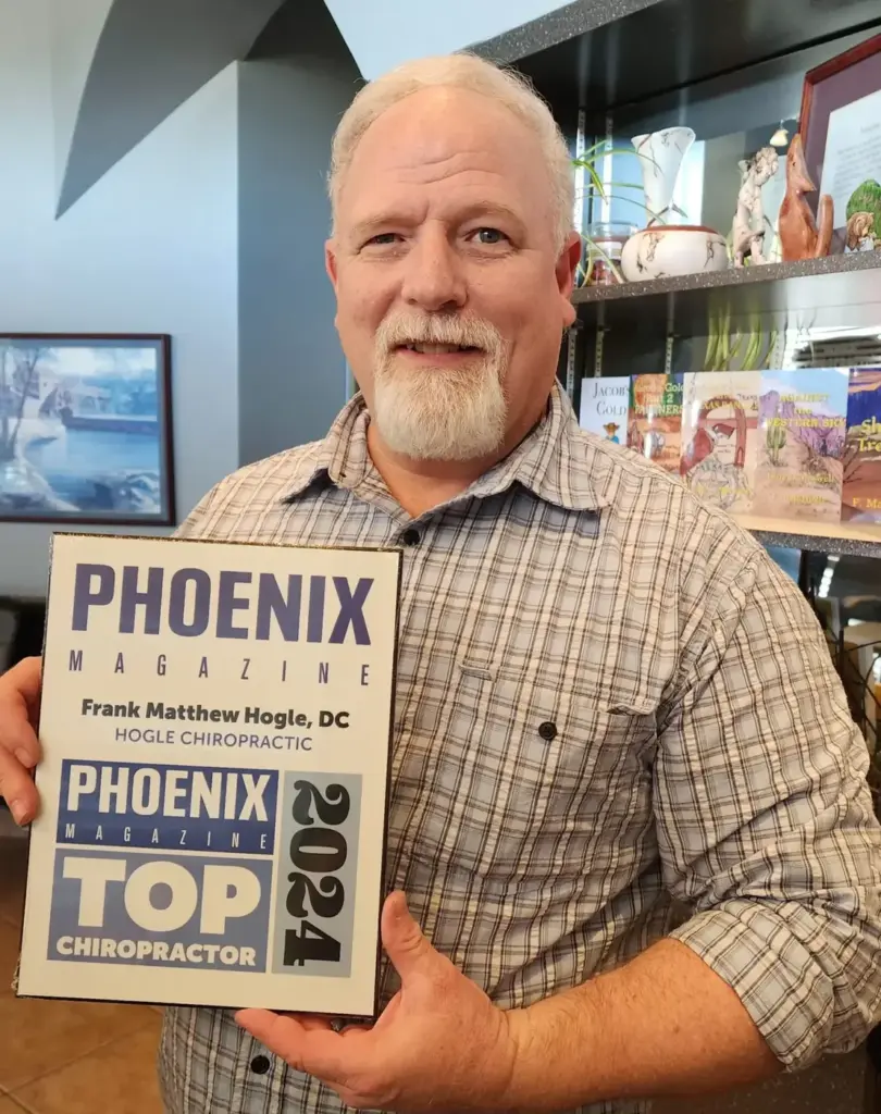 Dr. Matt Hogle smiling in the office, holding his Phoenix Magazine Top Chiropractor 2024 plaque